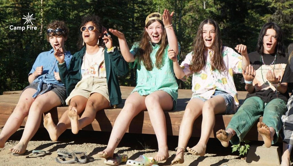 Camp Fire Alaska - Five young people sitting on a log laughing